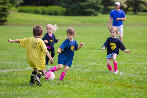 one boy and 3 girls are playing soccer in the field supervised by a parent coach